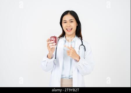 Attraktive Ärztin mit einem weißen, lächelnden Mantel und einem Apfel in der Hand. Fröhliche medizinische Ernährungsberaterin empfiehlt eine gesunde Ernährung für einen Patienten. Stockfoto