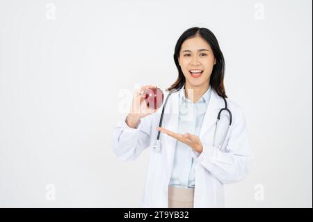 Attraktive Ärztin mit einem weißen, lächelnden Mantel und einem Apfel in der Hand. Fröhliche medizinische Ernährungsberaterin empfiehlt eine gesunde Ernährung für einen Patienten. Stockfoto