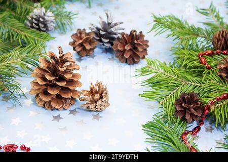 Braune Tannenzapfen mit Fichtenzweigen und roten Perlen auf blauem Hintergrund mit Sternen. Weihnachten, Neujahr, Feiertag, Winter. Kopierbereich Stockfoto