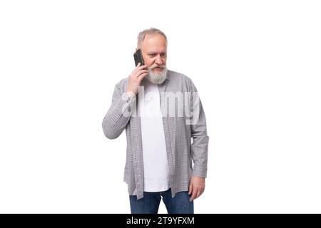 Ein gutaussehender reifer Mann mit weißem Bart und Schnurrbart in einem lässigen, bequemen Hemd spricht am Telefon Stockfoto