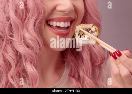 Eine junge Frau mit roten Nägeln und rosa Haaren isst Sushi aus nächster Nähe. Stockfoto