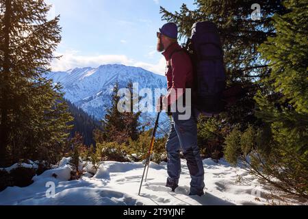 Ein männlicher Tourist wandert in den Bergen. Bärtiger Reisender mit großem Rucksack. Schönes Wetter an einem sonnigen Wintertag draußen in den Bergen Stockfoto