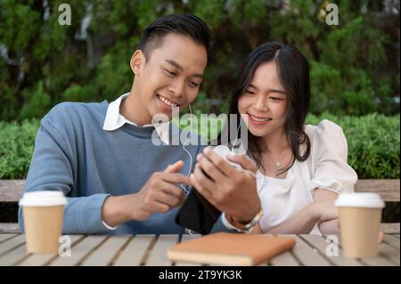 Junges asiatisches Paar, das gemeinsam Musik hört und sich im grünen Park amüsiert. Paarungskonzept. Stockfoto