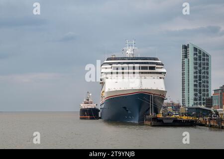 Ein riesiges Kreuzfahrtschiff, das in Liverpool, England angedockt wurde, mit einem kleinen Schlepper daneben. Der Tag ist bewölkt Stockfoto