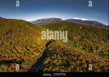 Blick aus der Vogelperspektive auf die Berge, die von Buchenwäldern mit den Farben Rot, Gelb, Orange und Grün des Herbstlaub im Maiella-Nationalpark bedeckt sind Stockfoto