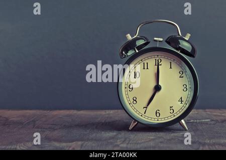 Es ist schon sieben Uhr, Zeit zum Frühstück aufzuwachen, Vintage alter schwarzer Metallic Wecker auf Vintage Holz Hintergrund Atmosphäre Stockfoto