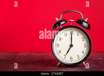 Es ist schon sieben Uhr, Zeit für die Liebe aufzuwachen, Vintage alter schwarzer Metallic-Wecker auf rotem Hintergrund, valentinstag-Liebeskonzept Stockfoto