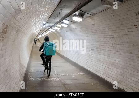 Ein Deliveroo-Radfahrer, der mit dem Fahrrad durch den Greenwich Foot Tunnel fährt. Der Tunnel verläuft unter der Themse und verbindet die Isle of Dogs mit Greenwich Stockfoto