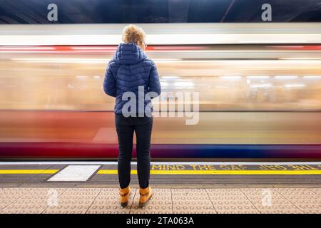 Ein Pendler steht auf dem Bahnsteig der Monument Tube Station in der Londoner U-Bahn, während eine U-Bahn durch den Bahnhof fährt Stockfoto