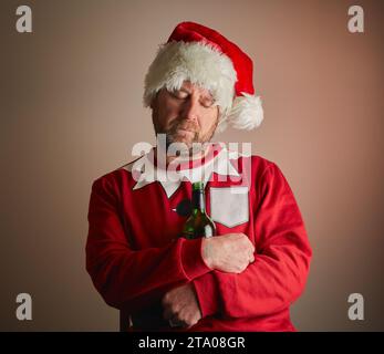 Ein Mann, der als Weihnachtsmann verkleidet ist, der eingeschlafen ist und eine Flasche Wein mit einem Gefälle hält. Modellversion verfügbar. Stockfoto