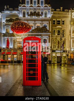 Ein Paar umarmt sich bei einer roten Telefonzelle vor der Fassade des Cartier-Ladens in Mayfair. Stockfoto