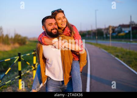 Glückliches lächelndes Paar, das den Sonnenuntergang genießt. Der Mann trägt seine Frau zurück. Stockfoto