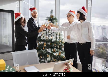 Multiethnische Geschäftsleute in Santa Hats, die Champagner mit Kollegen klappern Stockfoto