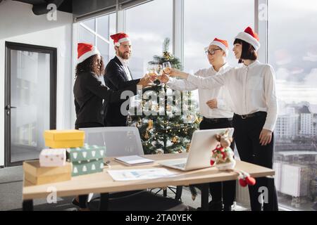 Multiethnische Geschäftsleute in Santa Hats, die Champagner mit Kollegen klappern Stockfoto