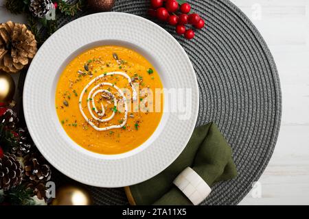 Karotten- und Kürbiscreme mit Sahne und Nüssen. Weihnachtsessen werden auf einem Tisch serviert, der mit Weihnachtsmotiven dekoriert ist. Stockfoto