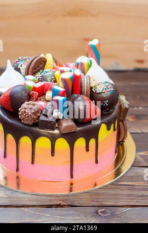 Farbenfroher, reich verzierter rosafarbener Kuchen mit Süßigkeiten, Eis, Lutscher, Gelee, Erdbeeren und Cupcakes auf rustikalem Hintergrund Stockfoto