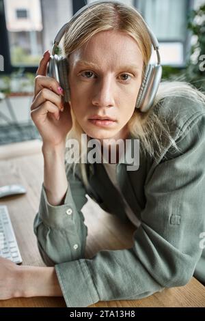 Porträt eines jungen androgynen Menschen in lässiger Kleidung mit Kopfhörern, die in die Kamera schauen, geschäftlich Stockfoto