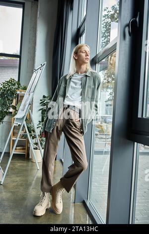 Vertikale Aufnahme einer langhaarigen, nicht binären Person, die im Büro posiert und wegblickt, Geschäftskonzept Stockfoto