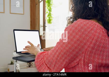 Rückansicht einer nicht erkennbaren jungen Frau drinnen, die am Schreibtisch sitzt, mit der Online-Suche auf Laptop nach Ticketangeboten für Urlaubsflug beschäftigt ist, Handel Conce Stockfoto