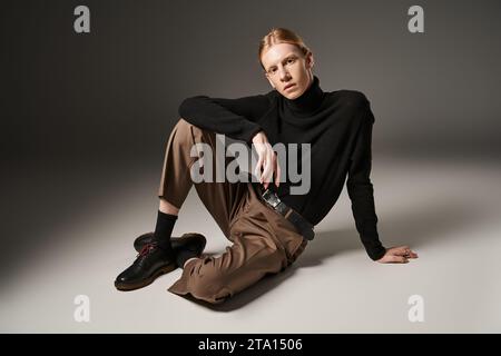 Junge nicht binäre Person mit schwarzem Rollkragen, die auf dem Boden sitzt und die Kamera ansieht, Modekonzept Stockfoto