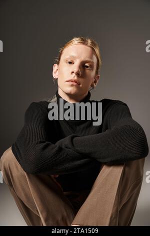 Vertikale Aufnahme einer jungen nicht binären Person, die mit überkreuzten Beinen auf dem Boden sitzt und in die Kamera blickt Stockfoto