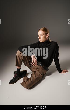 Gut aussehende, nicht binäre Person in schwarzem Rollkragen und brauner Hose, die auf dem Boden sitzt, Mode Stockfoto