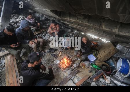 Khan Yunis, Palästinensische Gebiete. November 2023. Während des vorübergehenden Waffenstillstands zwischen Israel und der Hamas sitzen Palästinenser um Feuer, umgeben von der Zerstörung im Dorf Khuza·a in der Nähe des Grenzzauns zwischen Israel und dem südlichen Gazastreifen. Quelle: Mohammed Talatene/dpa/Alamy Live News Stockfoto