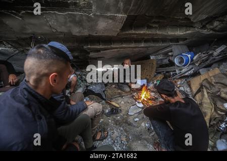 Khan Yunis, Palästinensische Gebiete. November 2023. Während des vorübergehenden Waffenstillstands zwischen Israel und der Hamas sitzen Palästinenser um Feuer, umgeben von der Zerstörung im Dorf Khuza·a in der Nähe des Grenzzauns zwischen Israel und dem südlichen Gazastreifen. Quelle: Mohammed Talatene/dpa/Alamy Live News Stockfoto