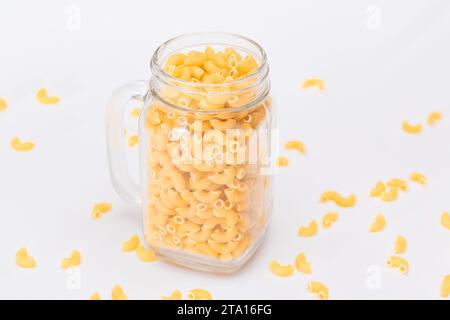 Ungekochte Chifferi Rigati Pasta in Glasglas auf weißem Hintergrund. Fett und ungesunde Lebensmittel. Verstreute Klassische Trockene Makkaroni. Italienische Kultur und Küche. Rohe Pasta Stockfoto