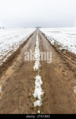 Schlammige Piste, die in einer schneebedeckten Landschaft zum Horizont führt. Stockfoto