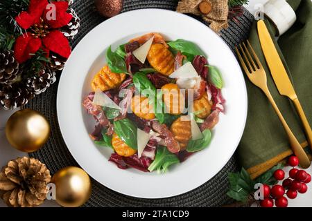 Gnocchi-Salat mit Speck und italienischem Käse. Weihnachtsessen werden auf einem Tisch serviert, der mit Weihnachtsmotiven dekoriert ist. Stockfoto