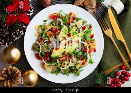 Argula-Salat mit Nudelbögen, Avocado, Kirschtomaten, Granatapfel und Sesam... Weihnachtsessen werden auf einem Tisch serviert, der mit Weihnachtsmotiven dekoriert ist. Stockfoto