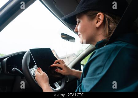 Eine Kurierin sitzt in einem Auto und schaut sich ein digitales Tablet an. Stockfoto