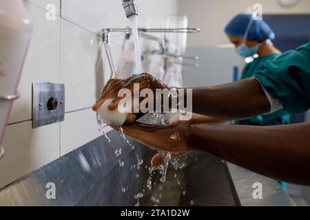 Hände diverser männlicher und weiblicher Chirurgen mit Gesichtsmasken, die Hände im Krankenhaus waschen Stockfoto