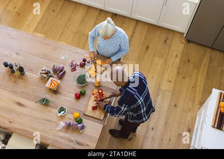 Diverse Seniorenpaare schneiden Butternusskürbis und roten Pfeffer in der Küche Stockfoto
