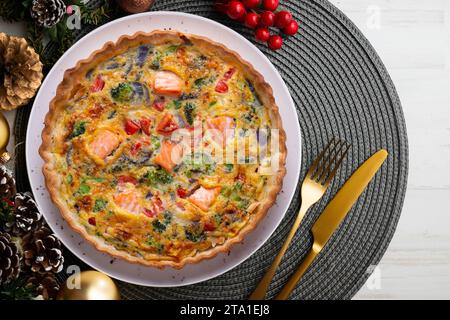 Traditionelle Lachsquiche mit Brokkoli und Gemüse. Weihnachtsessen werden auf einem Tisch serviert, der mit Weihnachtsmotiven dekoriert ist. Stockfoto