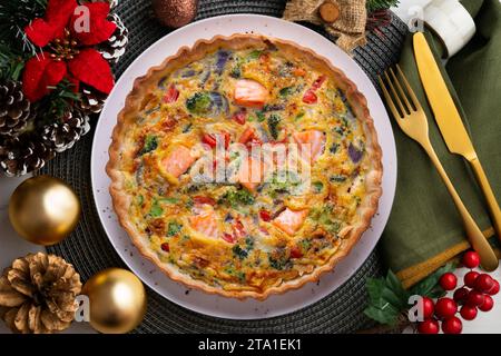 Traditionelle Lachsquiche mit Brokkoli und Gemüse. Weihnachtsessen werden auf einem Tisch serviert, der mit Weihnachtsmotiven dekoriert ist. Stockfoto