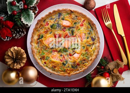 Traditionelle Lachsquiche mit Brokkoli und Gemüse. Weihnachtsessen werden auf einem Tisch serviert, der mit Weihnachtsmotiven dekoriert ist. Stockfoto