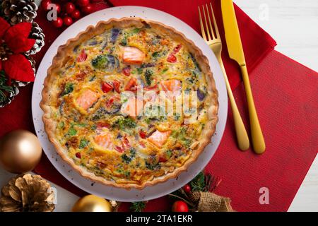 Traditionelle Lachsquiche mit Brokkoli und Gemüse. Weihnachtsessen werden auf einem Tisch serviert, der mit Weihnachtsmotiven dekoriert ist. Stockfoto