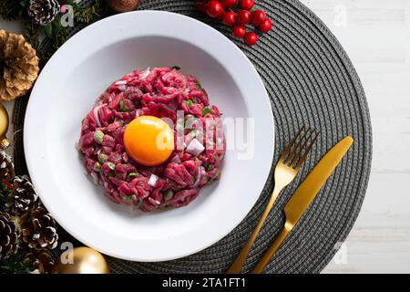 Traditionelles Steak-Tartar mit Rindfleisch und Eigelb. Weihnachtsessen werden auf einem Tisch serviert, der mit Weihnachtsmotiven dekoriert ist. Stockfoto