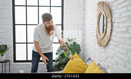 Der hübsche junge rothaarige Mann wacht auf und fängt morgens Sonnenlicht im Schlafzimmer seiner Wohnung ein, während er sich um das Bett kümmert und konzentriert Stockfoto