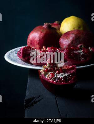 Frische Granatäpfel auf alten rustikalen Tisch Stillleben in dunklen Tönen. Reife und saftige Granatapfelfrüchte in Nahaufnahme auf schwarzem Hintergrund. Stockfoto