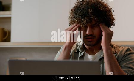 Müder arabischer Freiberufler, Geschäftsmann, der von der Hausküche aus arbeitet, leidet unter Kopfschmerzen. Kranker, erschöpfter indischer Student, der mit Laptop erschöpft war Stockfoto