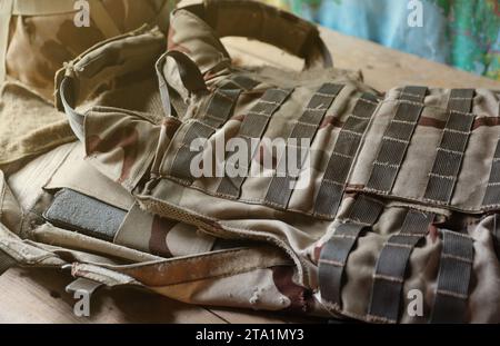 Ein Militärhelm eines ukrainischen Soldaten mit einer schweren kugelsicheren Weste auf einem Holztisch im Innenraum des Kontrollpunktes Stockfoto