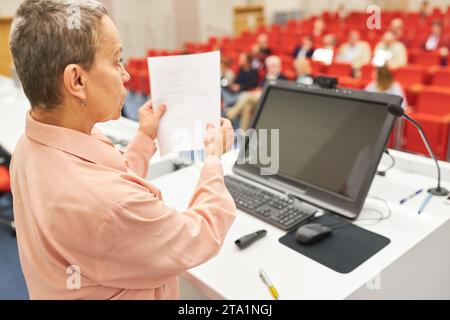 Reife Rednerin, die bei Geschäftskonferenzen Dokumente hält, während sie über das Publikum spricht Stockfoto