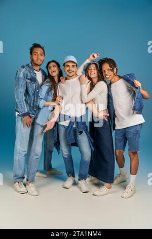 Gruppenporträt interrassischer Freunde in trendiger Kleidung und Denim-Kleidung vor blauem Hintergrund, in voller Länge Stockfoto