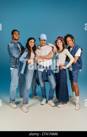 Die ganze Länge von interrassischen Freunden in trendigen und Denim-Kleidern vor blauem Hintergrund, griffiges Porträt Stockfoto