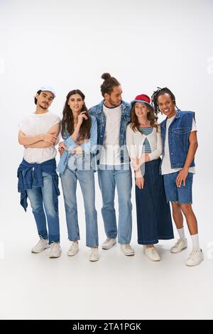 Die ganze Länge der interrassischen Freunde in trendigen Outfits und Jeansbekleidung im grauen Hintergrund Stockfoto