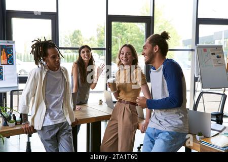 Glückliche Frau mit Kaffee, die in der Nähe eines multiethnischen Teams über Startup im Büro spricht Stockfoto