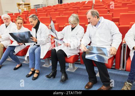 Ärzte, die im Publikum einer medizinischen Konferenz sitzen und Röntgenaufnahmen untersuchen, während sie auf Stühlen im Auditorium sitzen Stockfoto